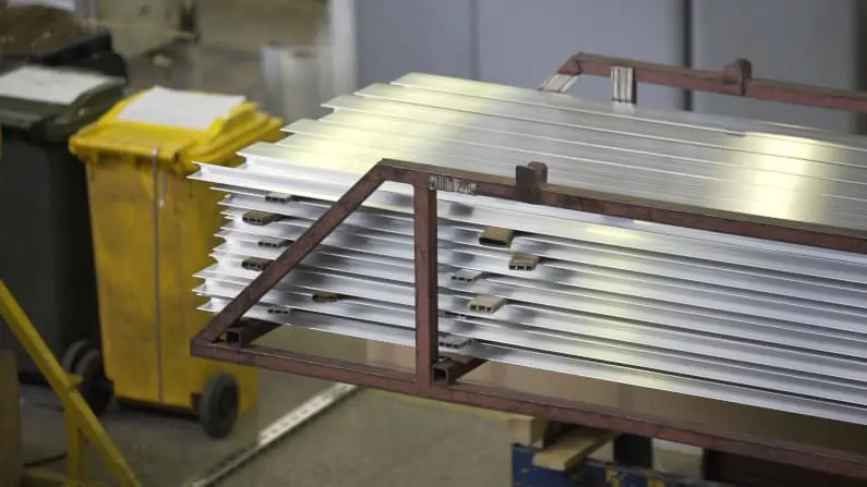 Crane beam moves stack of aluminum profiles in a factory warehouse. Heavy metallurgical industrial products, manufacturing business production concept